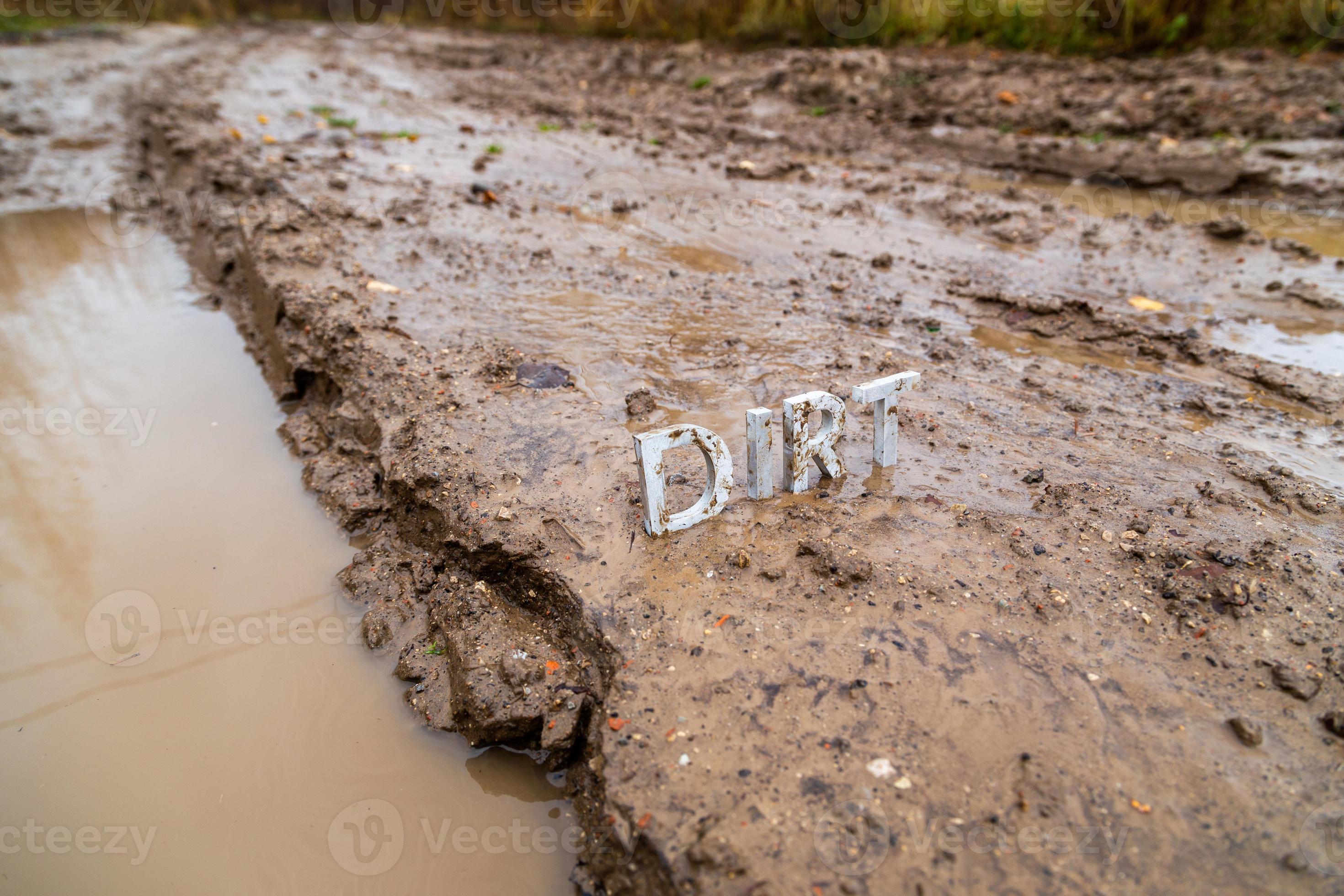 the word dirt composed of silver metal letters on wet clay surface