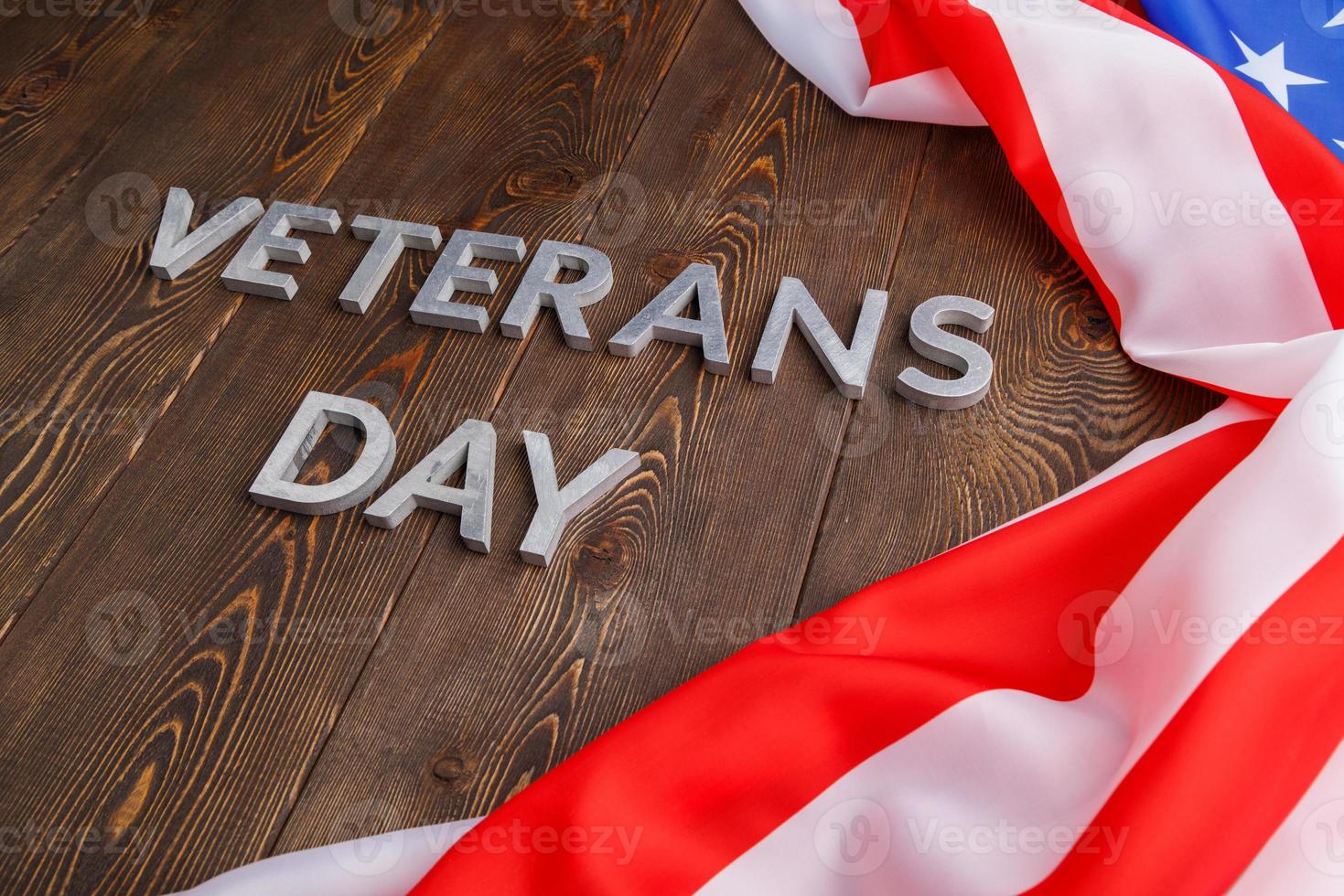 the words veterans day laid with silver metal letters on wooden board surface with crumpled usa flag at right side with diagonal perspective photo