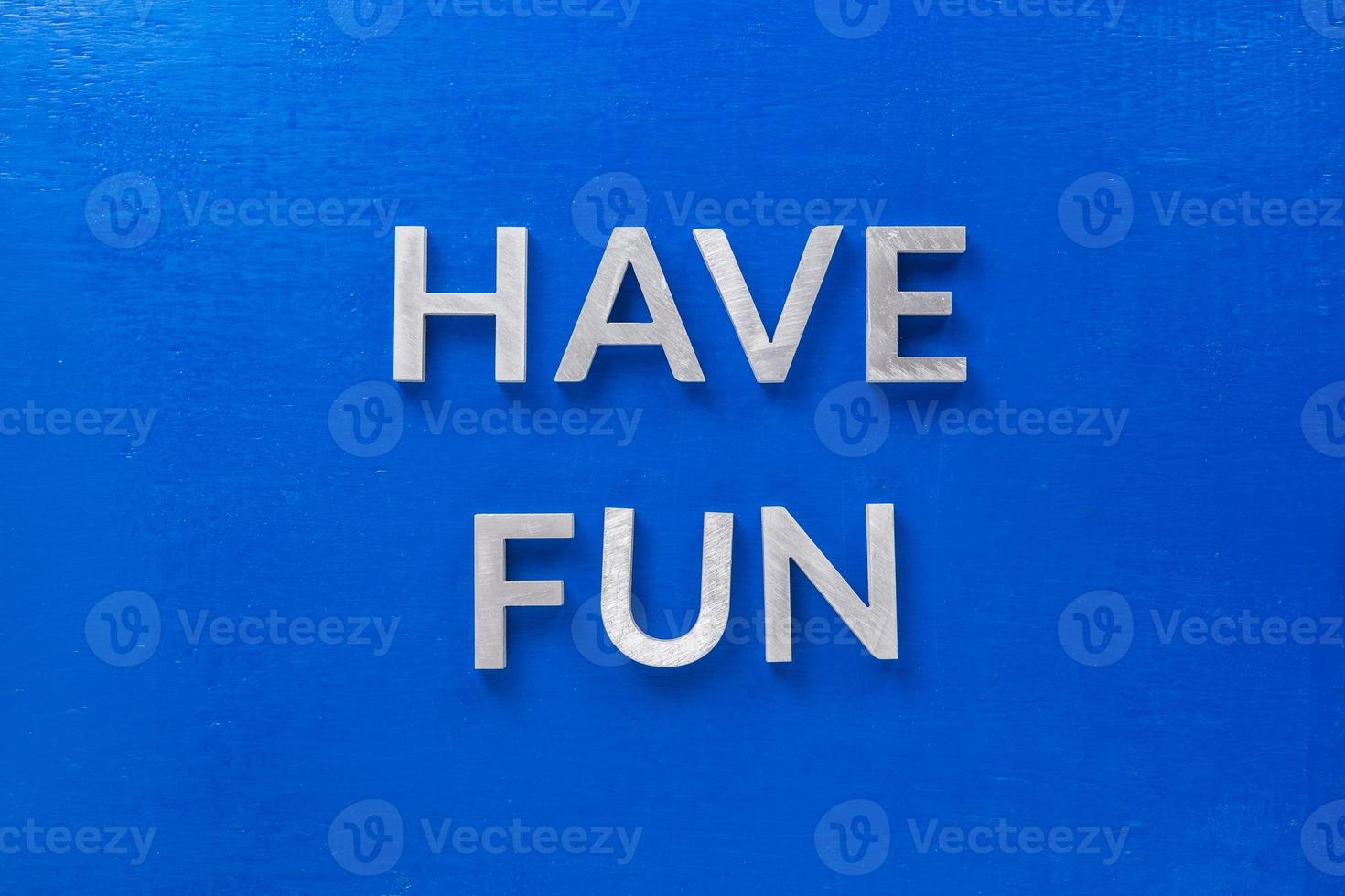 the words have fun laid with silver metal characters on blue painted wooden board in central flat lay composition photo