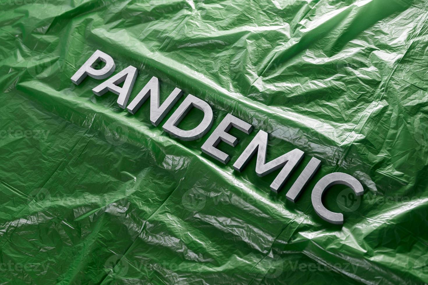 the word pandemic laid with silver letters on crumpled green plastic film - diagonal perspective composition with selective focus photo