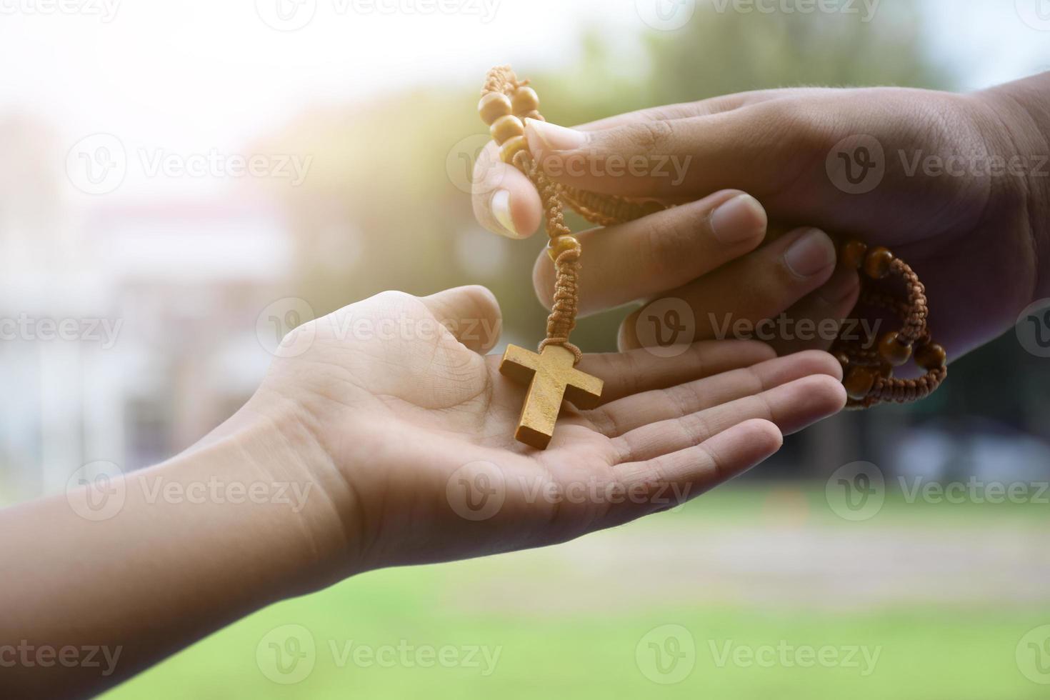 Closeup hands which offering wooden cross bead rosary to other people concept, soft and selective focus. photo