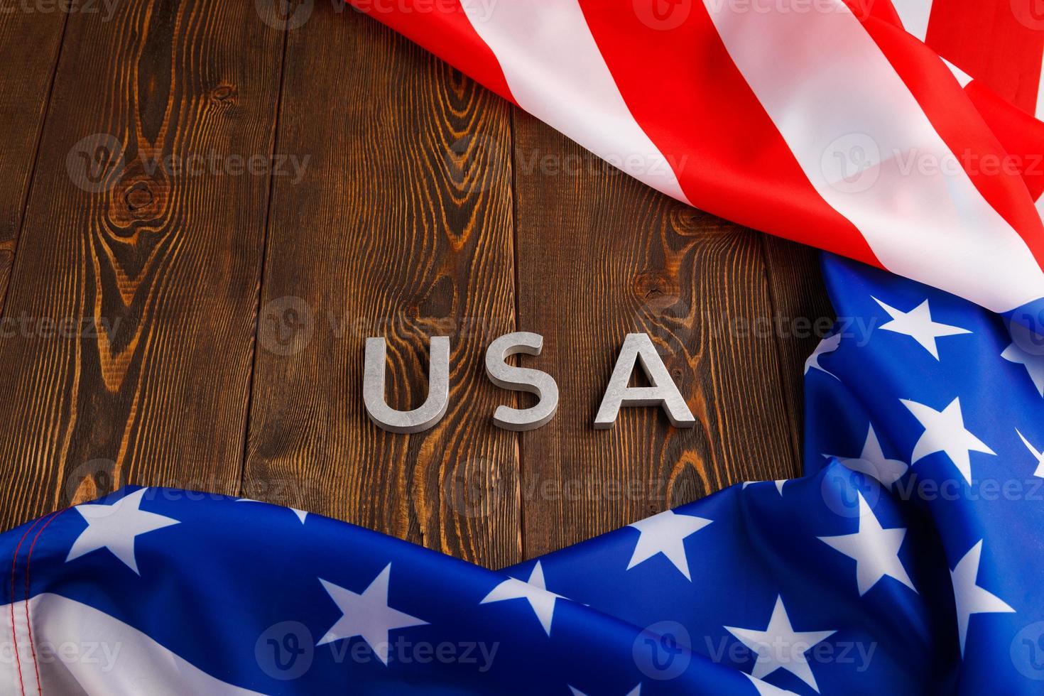 the word USA laid with silver metal letters on wooden board surface surrounded with crumpled flag of United States of America photo
