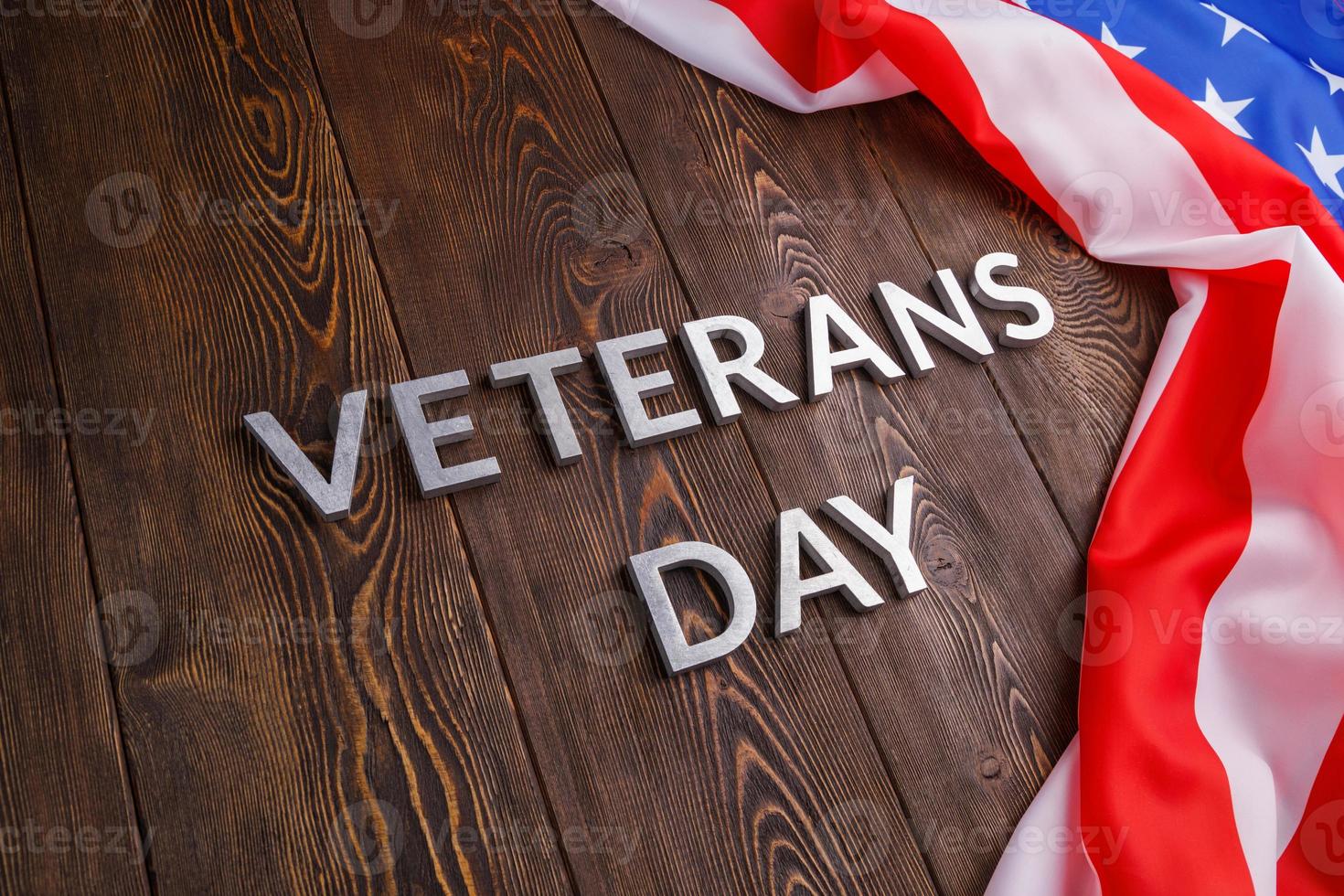 the words veterans day laid with silver metal letters on wooden board surface with crumpled usa flag at right side with diagonal perspective photo