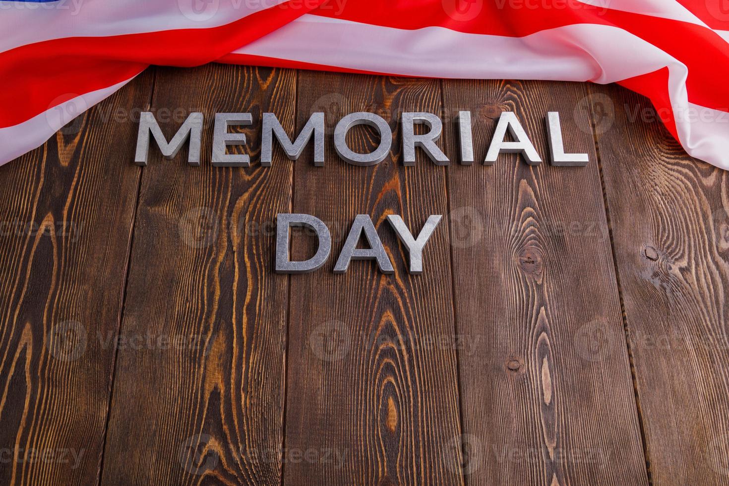the words memorial day laid with silver metal letters on wooden board surface with crumpled usa flag below photo