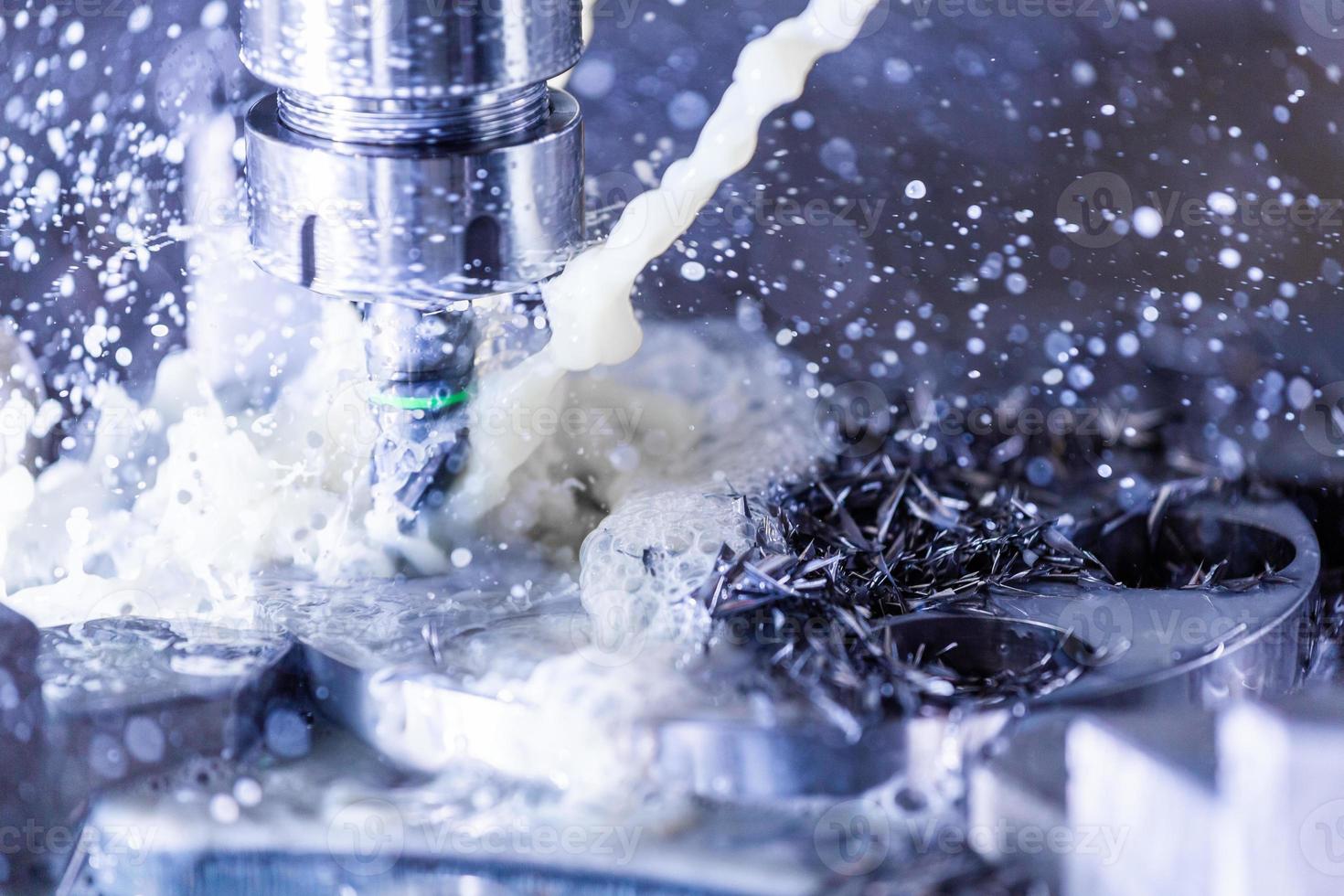 Close-up view of vertical cnc steel milling process with external water coolant streams, splashes and a lot of metal chips, high contrast photo