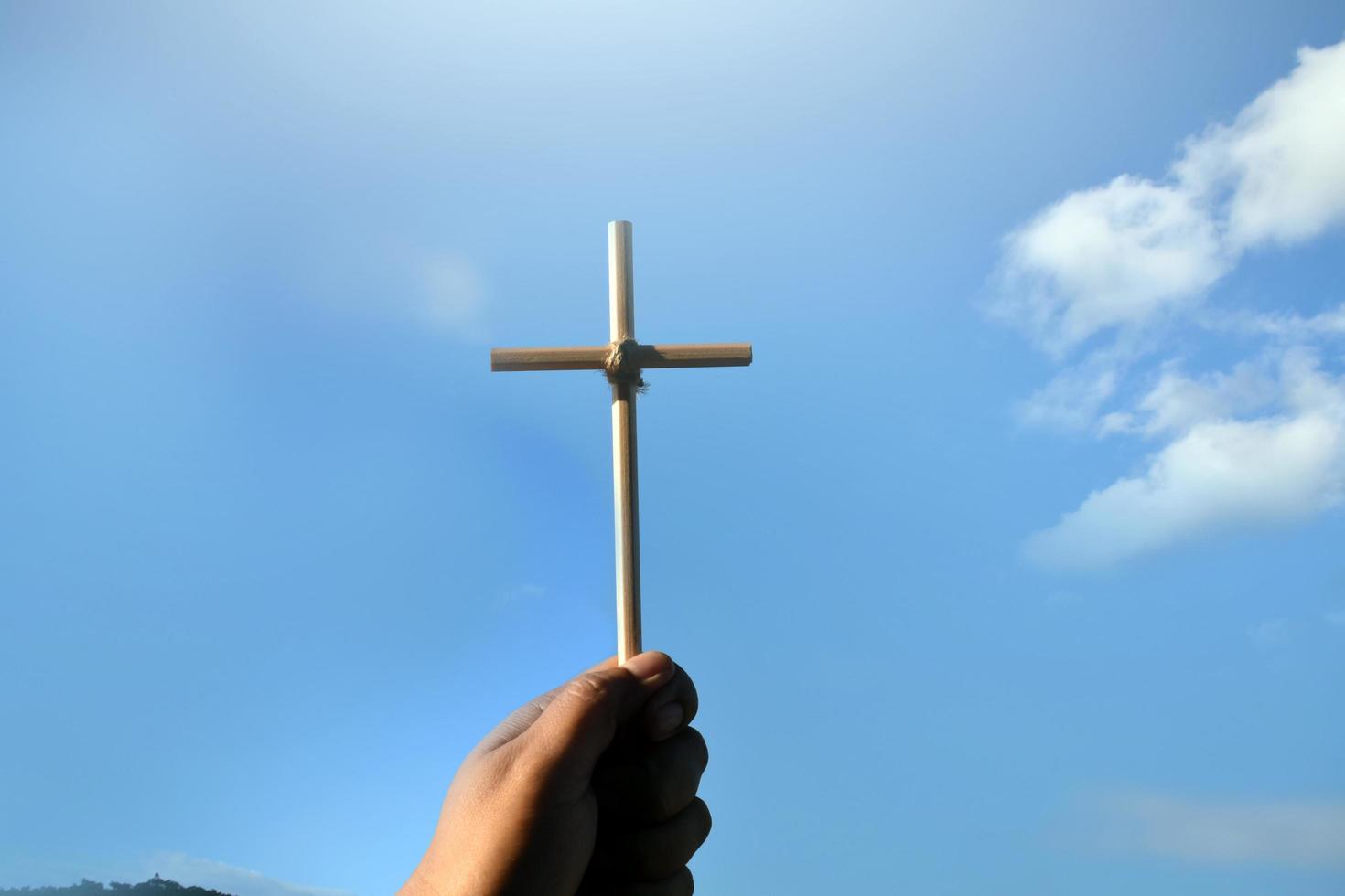 pequeña cruz de madera sosteniendo en la mano con fondo de cielo azul y nublado, concepto de amor, esperanza, verdad, fe, creer en Jesús, enfoque suave y selectivo. foto