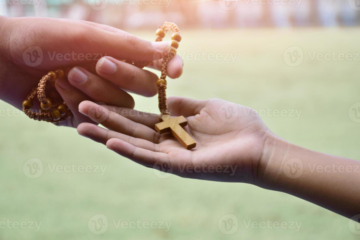 Closeup hands which offering wooden cross bead rosary to other people concept, soft and selective focus. photo