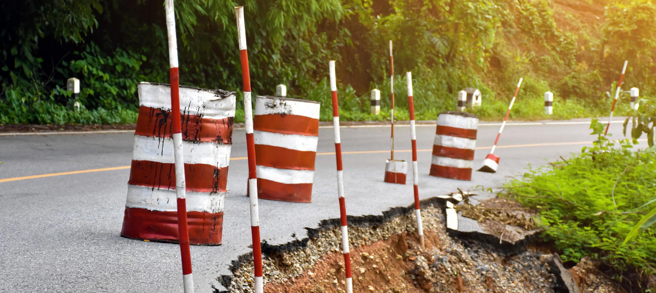 Cylindrical metal buckets and bamboo trunks painted red and white were placed and placed beside the paved road that had been eroded by rain to warn them to be careful when driving and avoiding danger. photo