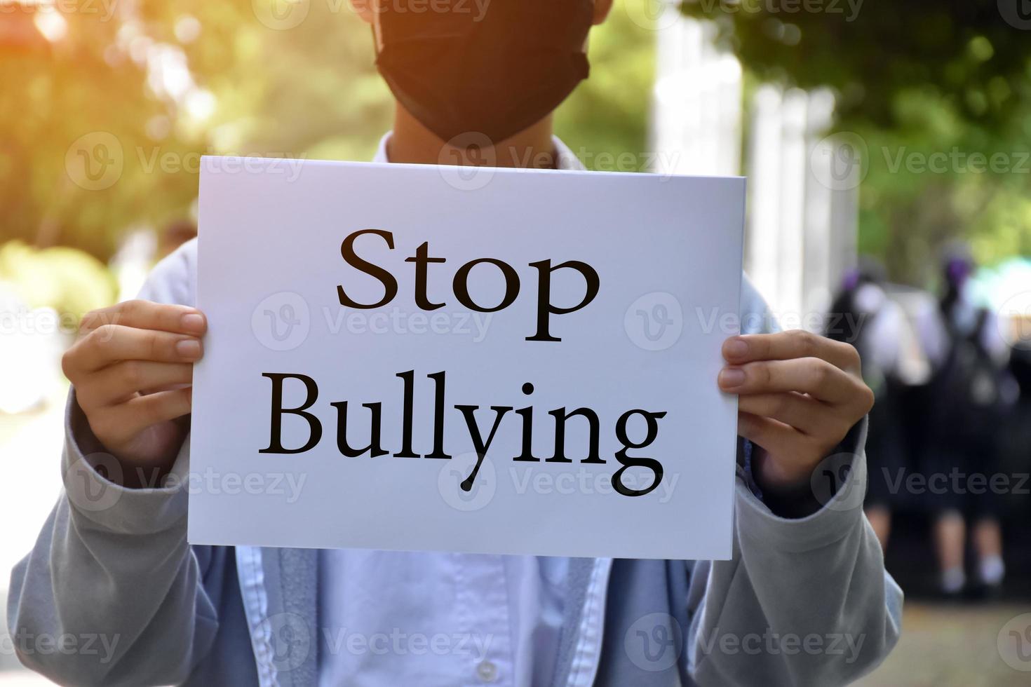 Asian boy student holds white paper which has texts Stop Bullying inside, concept for protesting or calling out all people around the world to stop bullying people in different countries. photo