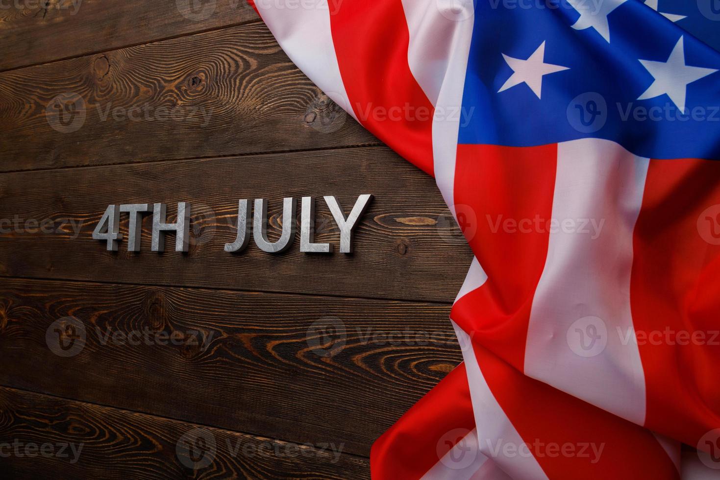 the words 4th july and crumpled usa flag on flat textured wooden surface background photo