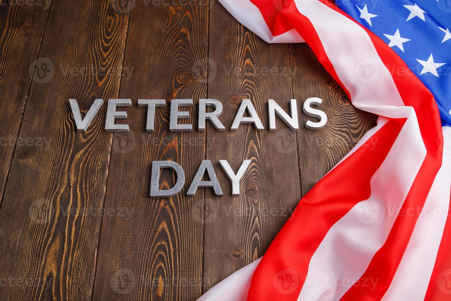 the words veterans day laid with silver metal letters on wooden board surface with crumpled usa flag photo