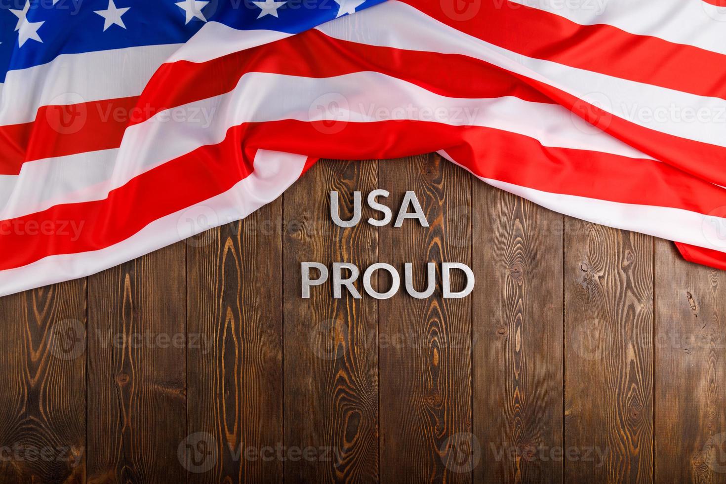 words USA proud laid with silver metal letters on brown wooden surface with flag of United States of America photo