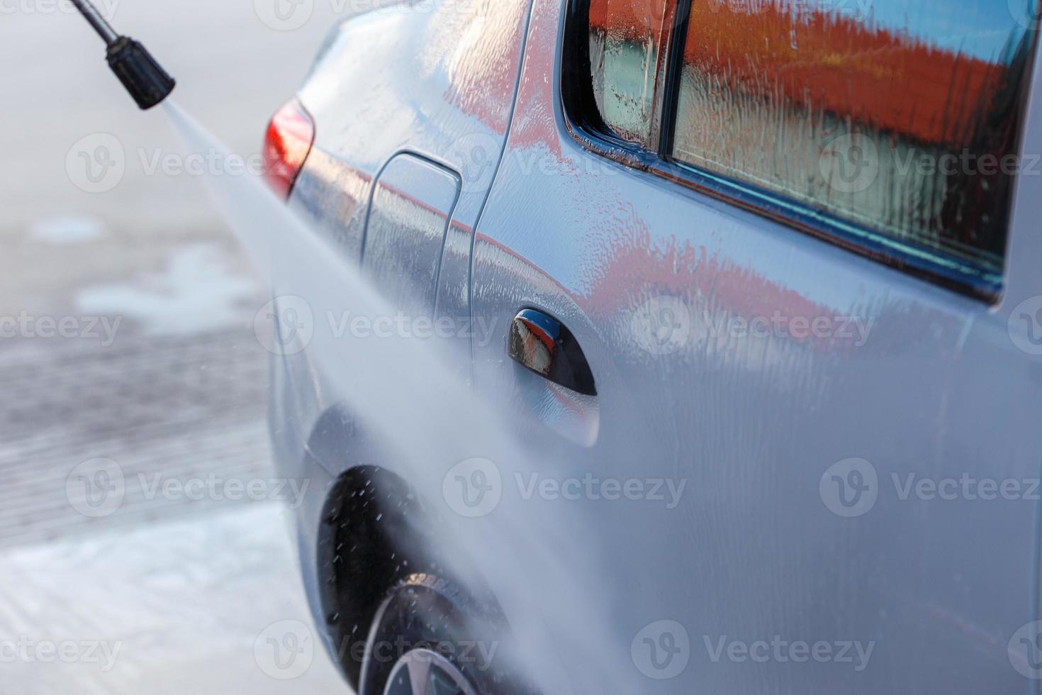 mano con lavadora de alta presión que lava el coche blanco en la estación pública de lavado de coches de autoservicio foto