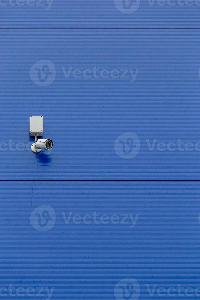 small white security camera on large blue steel silo wall photo