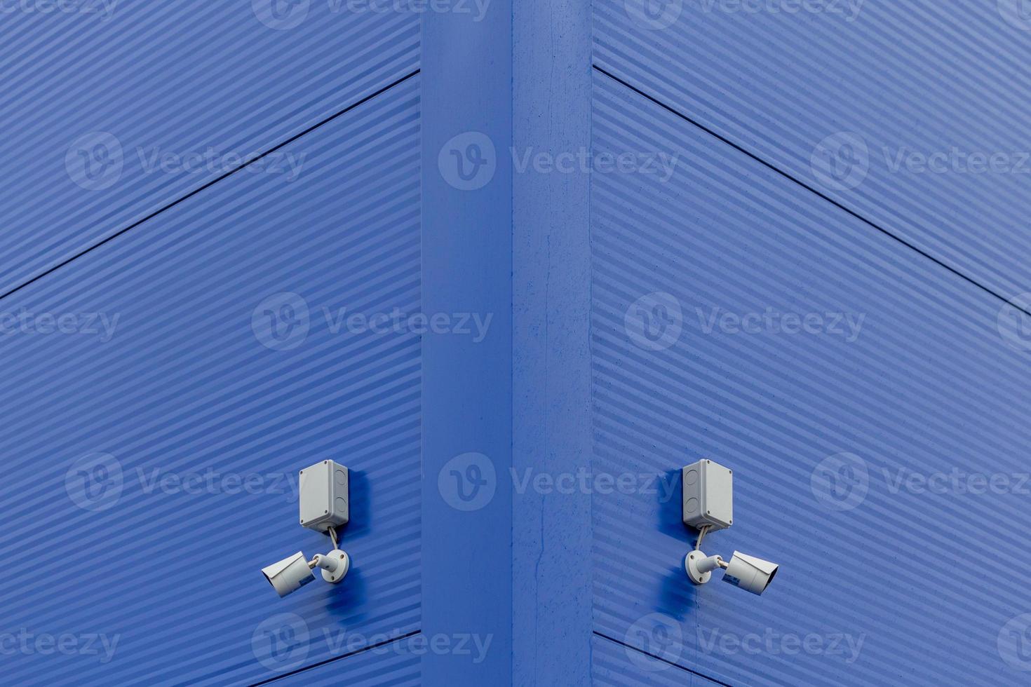 two small white security cameras on blue steel building corner photo