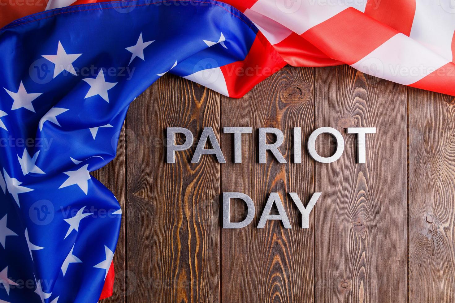 the words patriot day laid with silver metal letters on wooden board surface with crumpled usa flag photo
