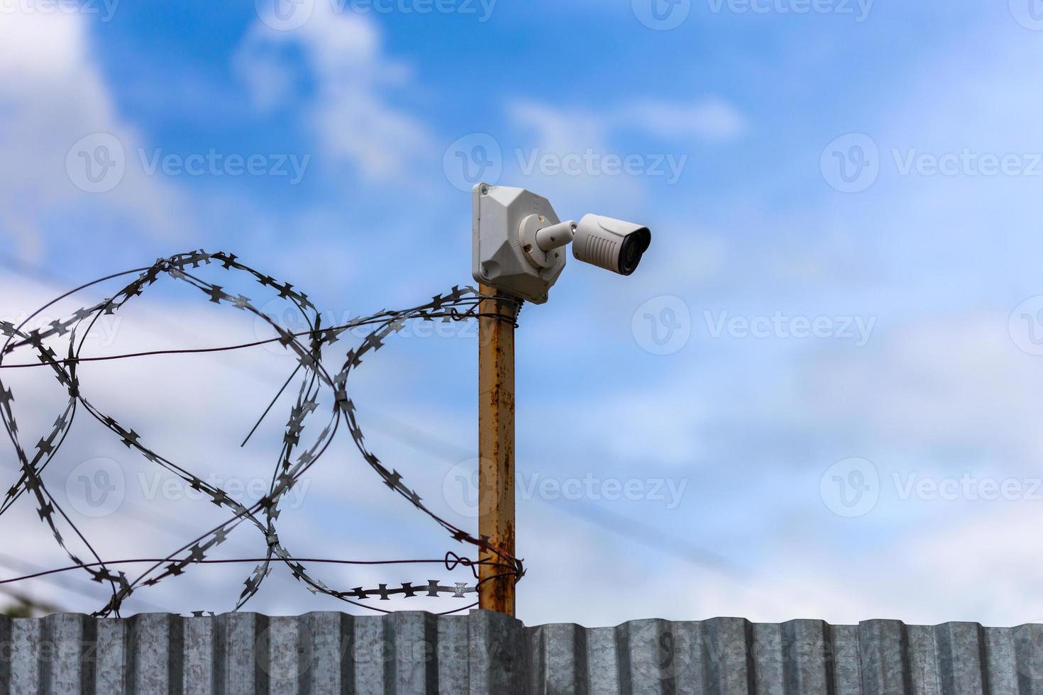 Profiled sheet fence with cheap surveillance camera and barbwire with selective focus. photo