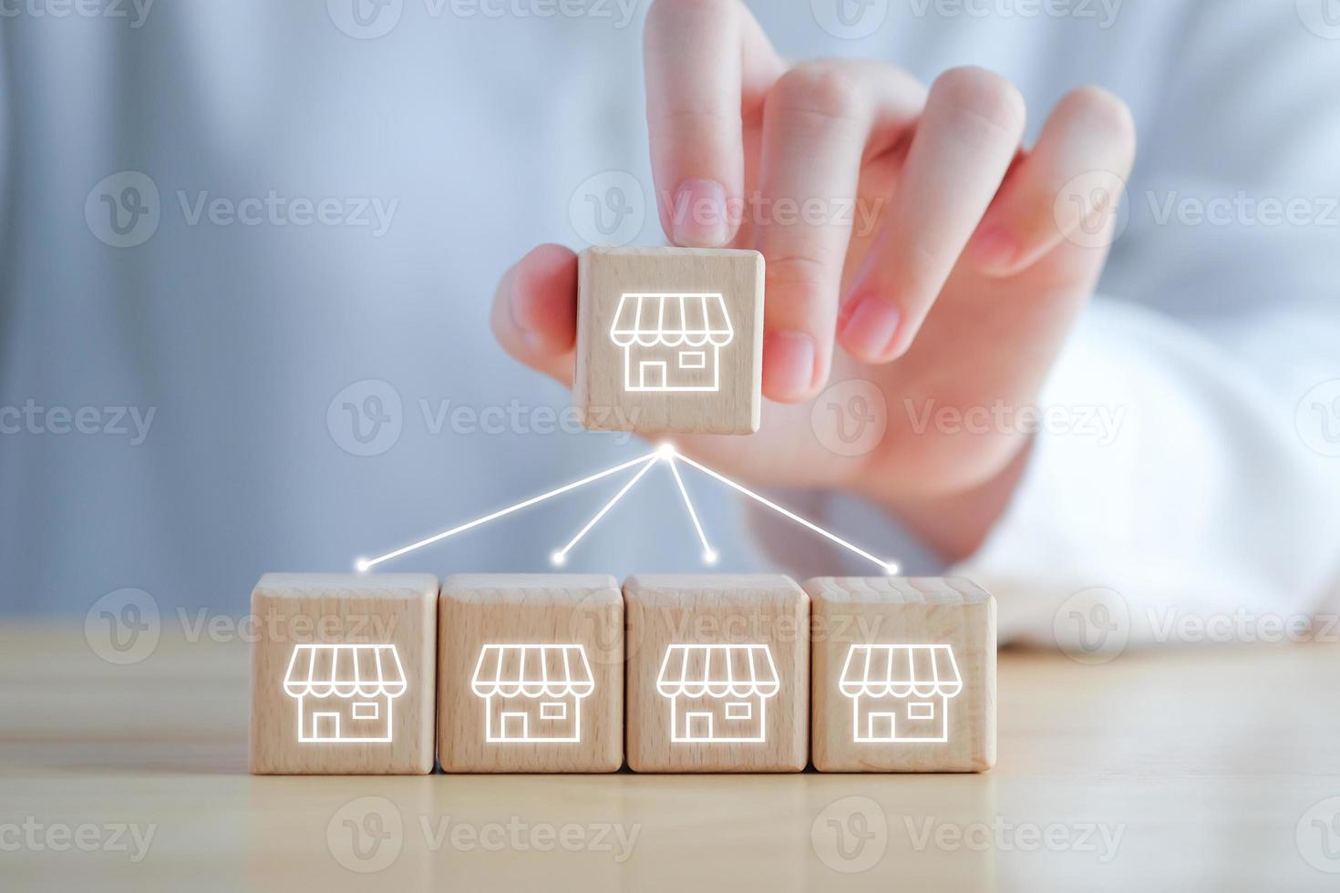 Franchise Business marketing concept. Hand holding franchise store icon on wooden block with line network connection to another store. photo