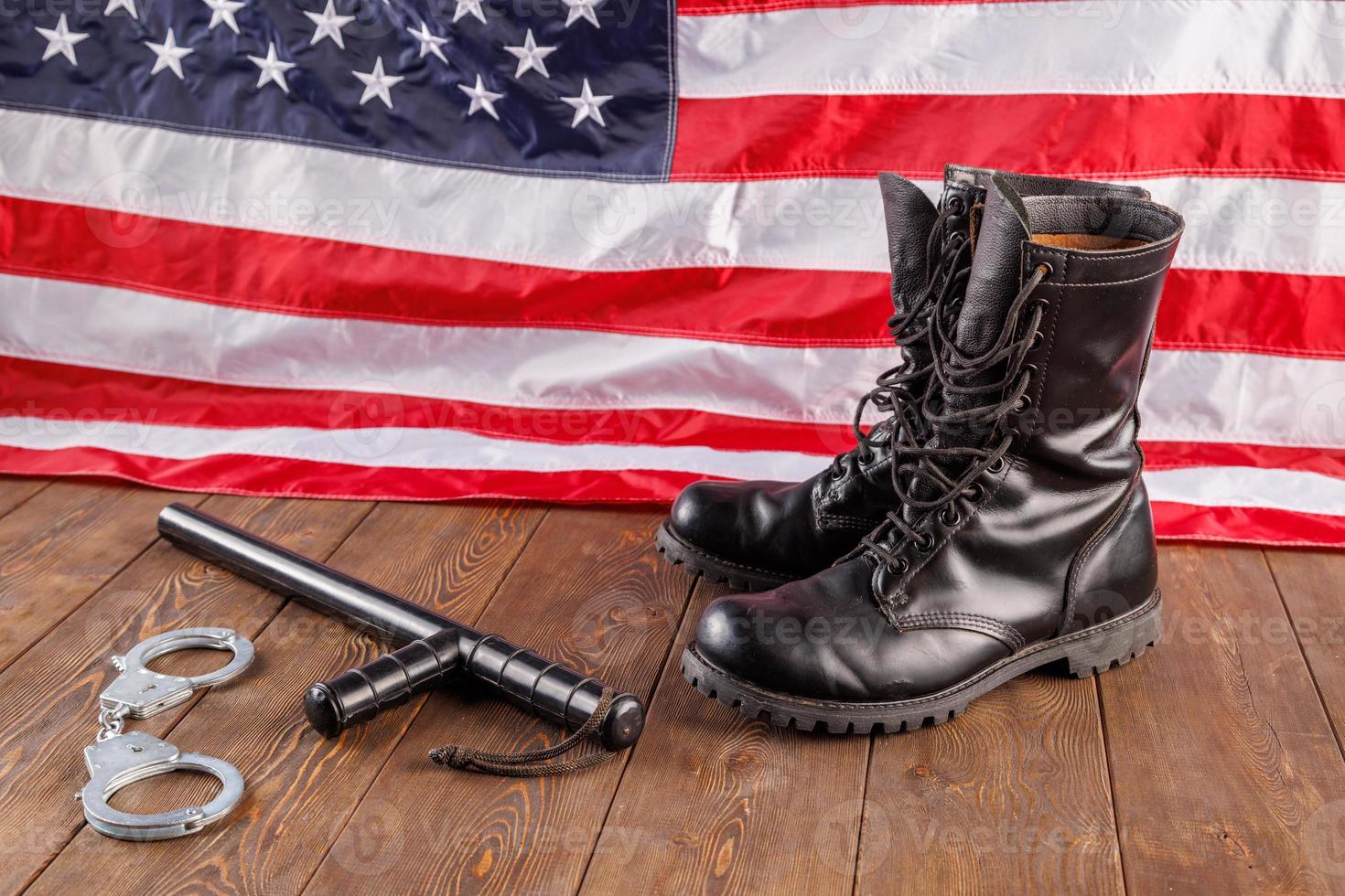 silver handcuffs, black boots and police baton near US flag on wooden surface photo