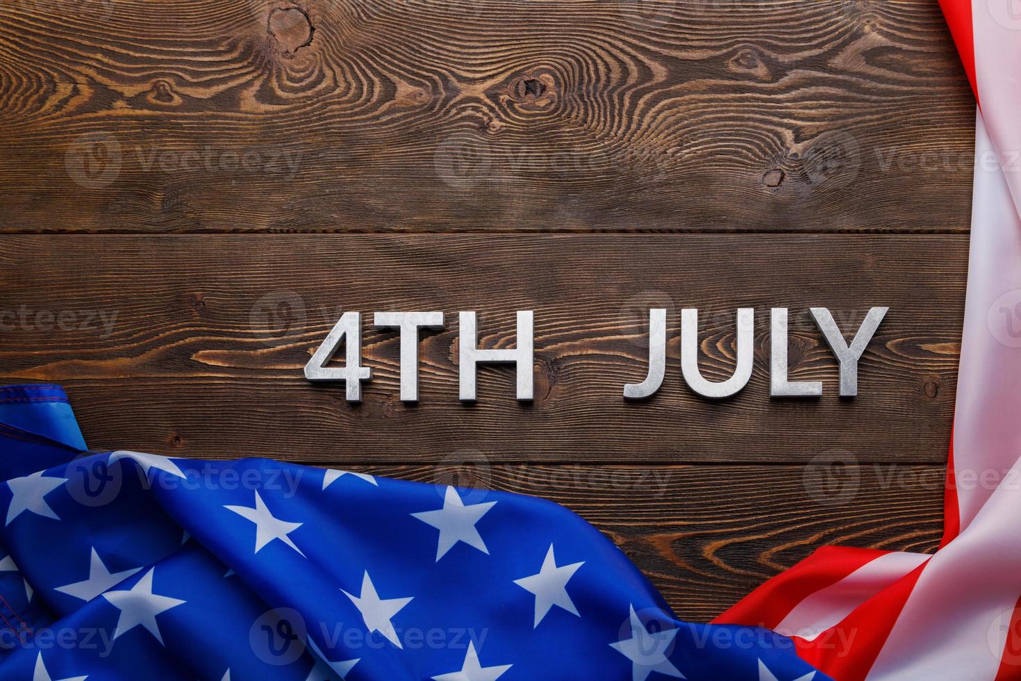 the words 4th july and crumpled usa flag on flat textured wooden surface background photo