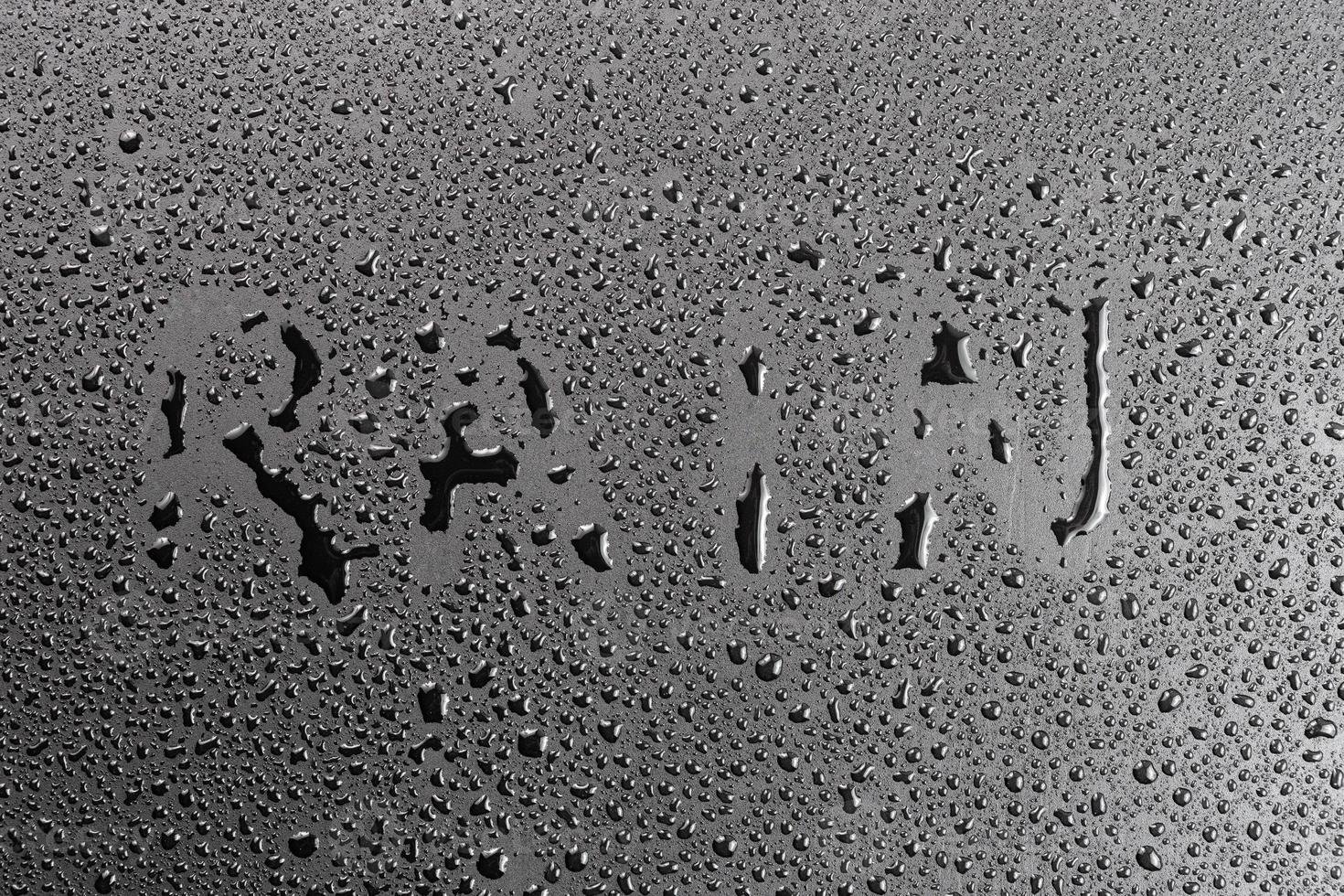 the word rain handwritten on matte black hydrophobic matte surface with water drops photo