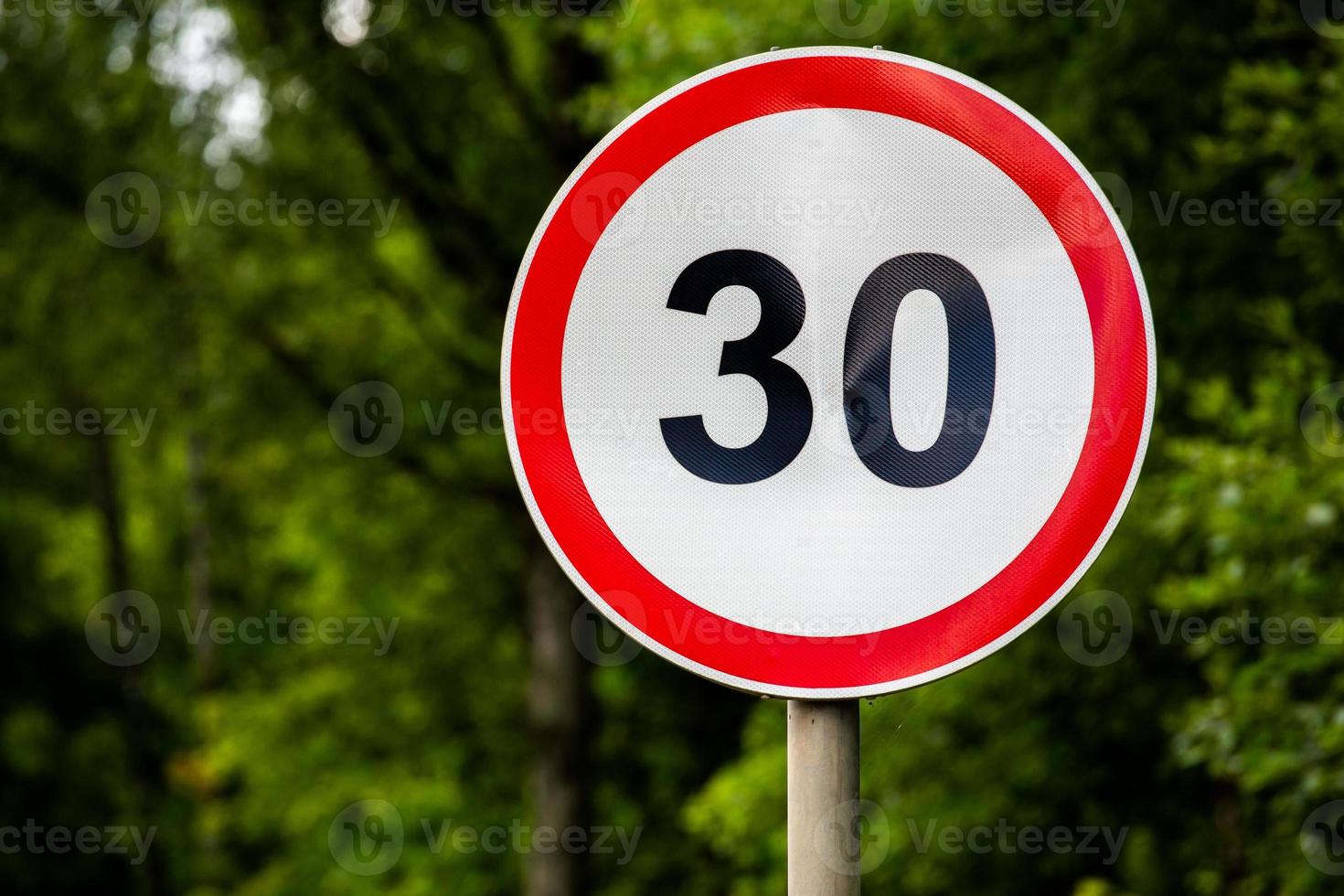 Road sign speed limit 30 kilometers per hour on green forest background with selective focus photo