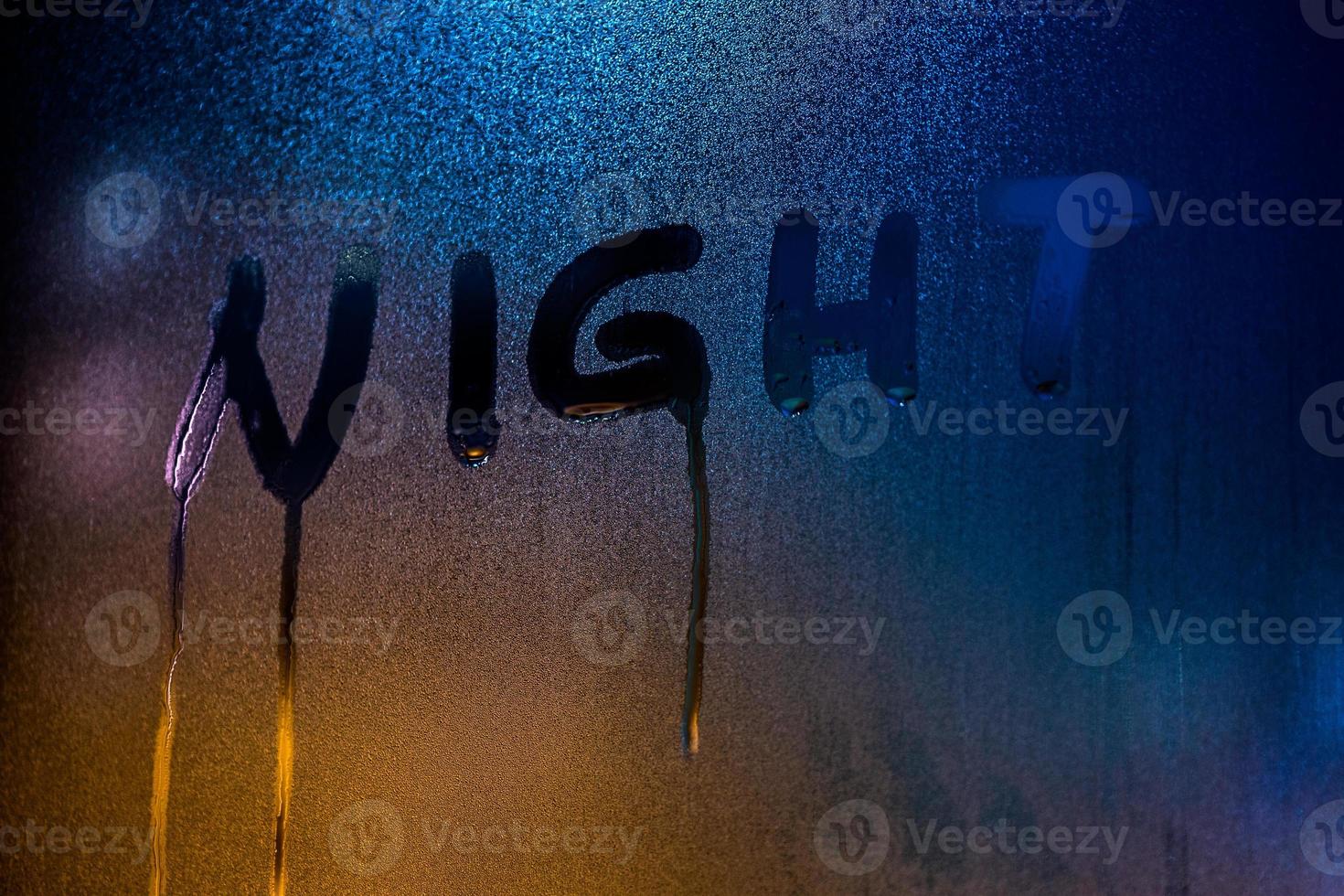 word NIGHT handwritten by finger on nightime wet window glass close-up photo