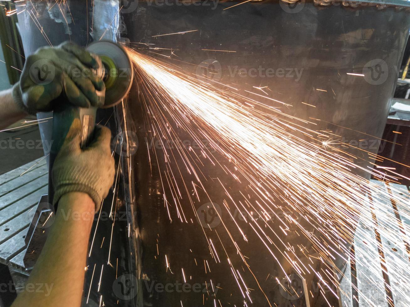 caucasian hands using an angle grinder on metal barrel vessel close-up with long sparks trails photo
