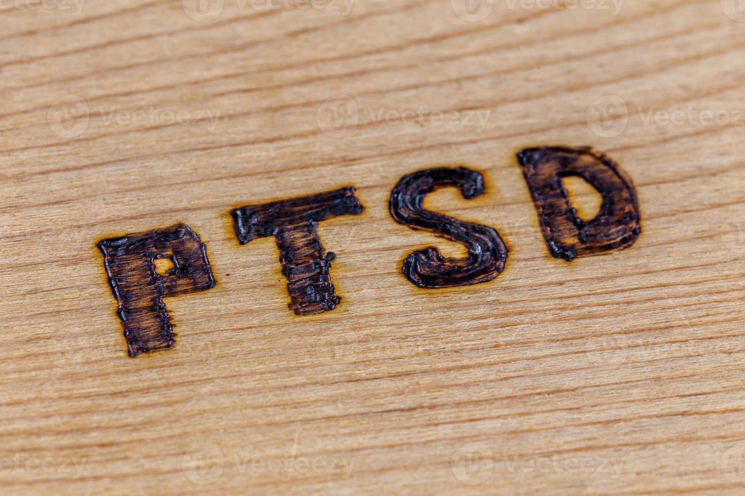 an abbreviation PTSD - post traumatic stress disorder - burned by hand on flat wooden board in diagonal composition photo