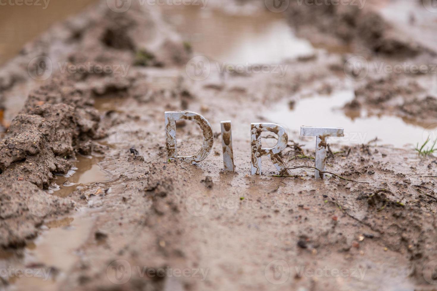 the word dirt composed of silver metal letters on wet clay surface photo