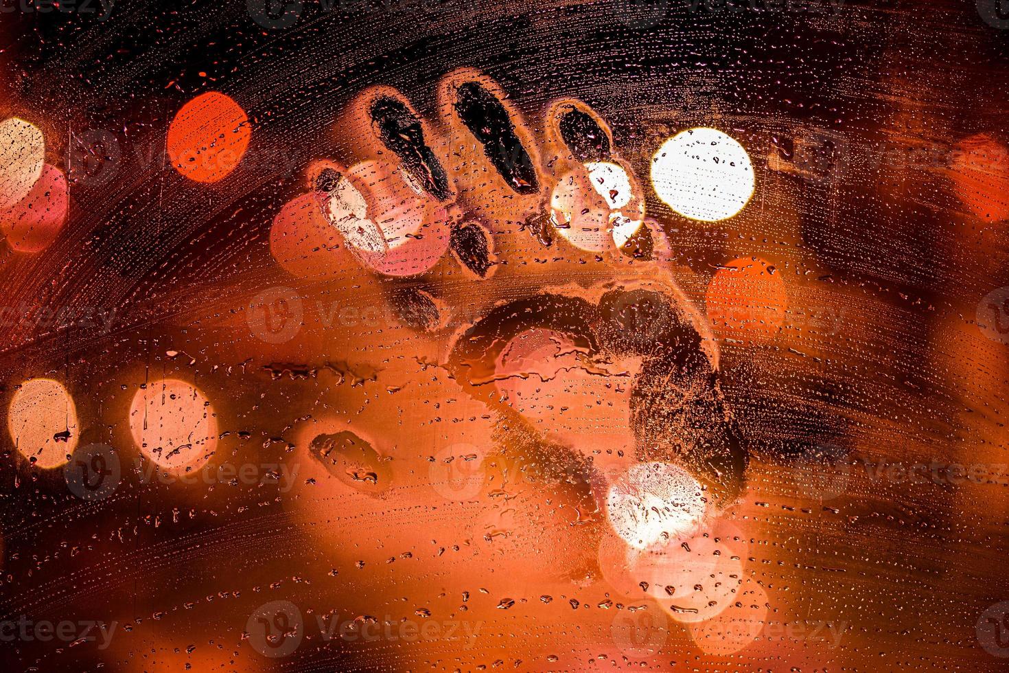 handprint on night wet glass in red colors with blurry street light in backround photo
