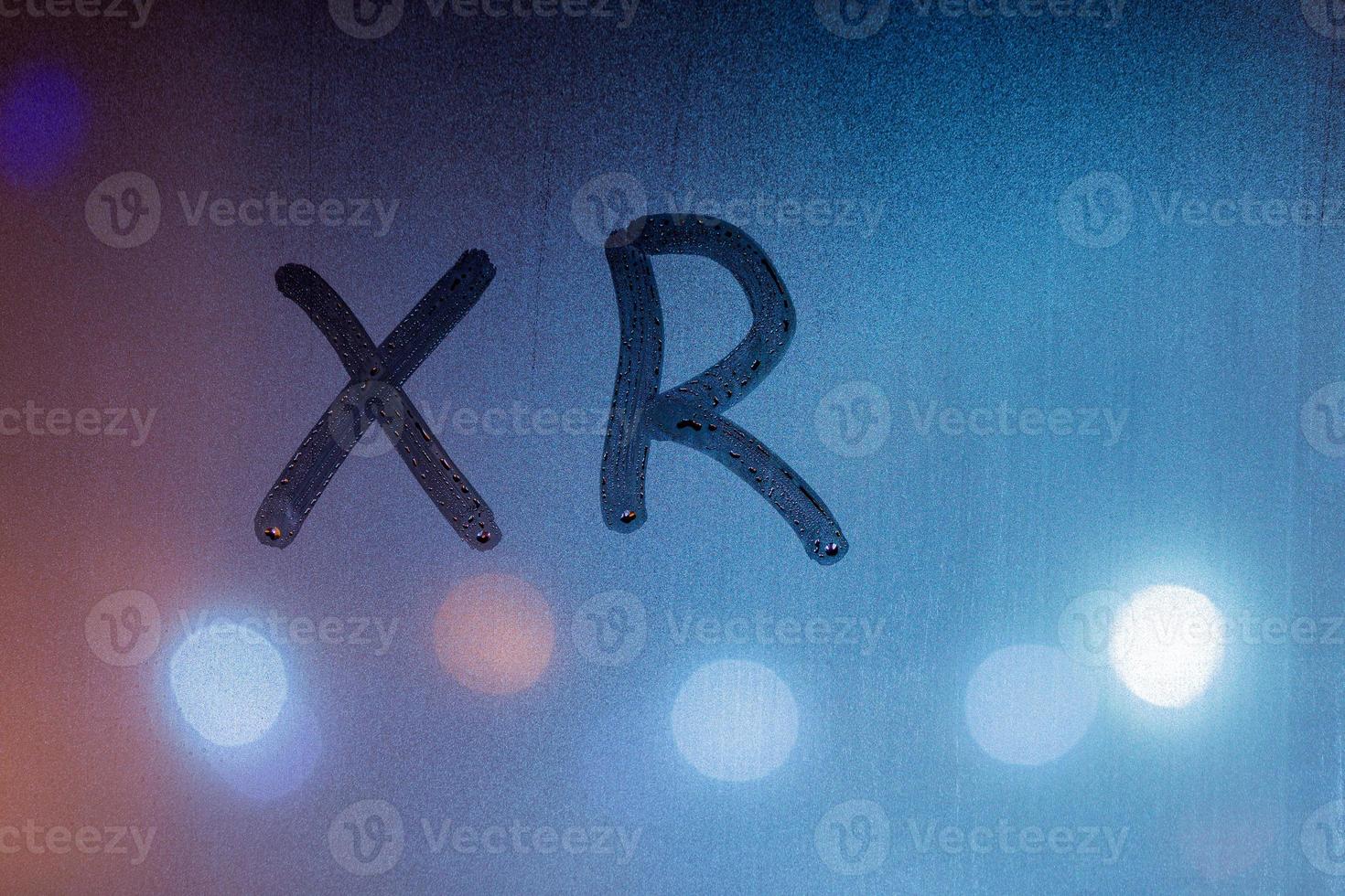 an abbreviation xr for extended reality handwritten on blue night wet window glass photo