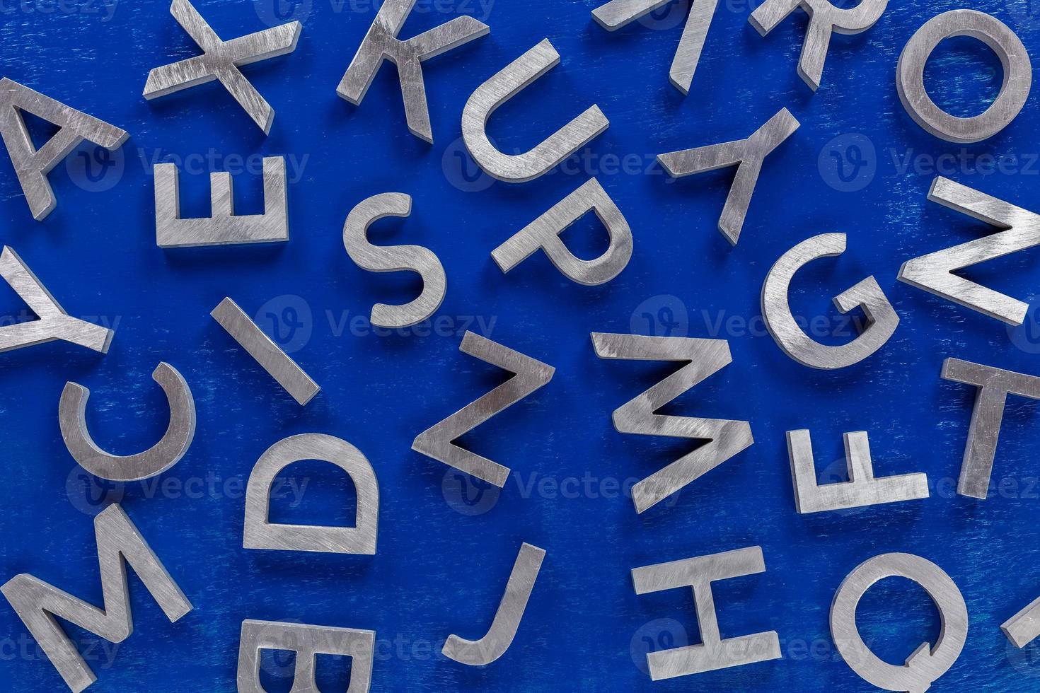 fondo plano abstracto de caracteres del alfabeto inglés de metal plateado sobre fondo azul. foto