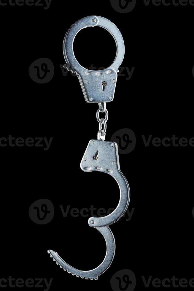 real zinc plated steel police handcuffs half-opened hanging vertically, isolated on black background photo