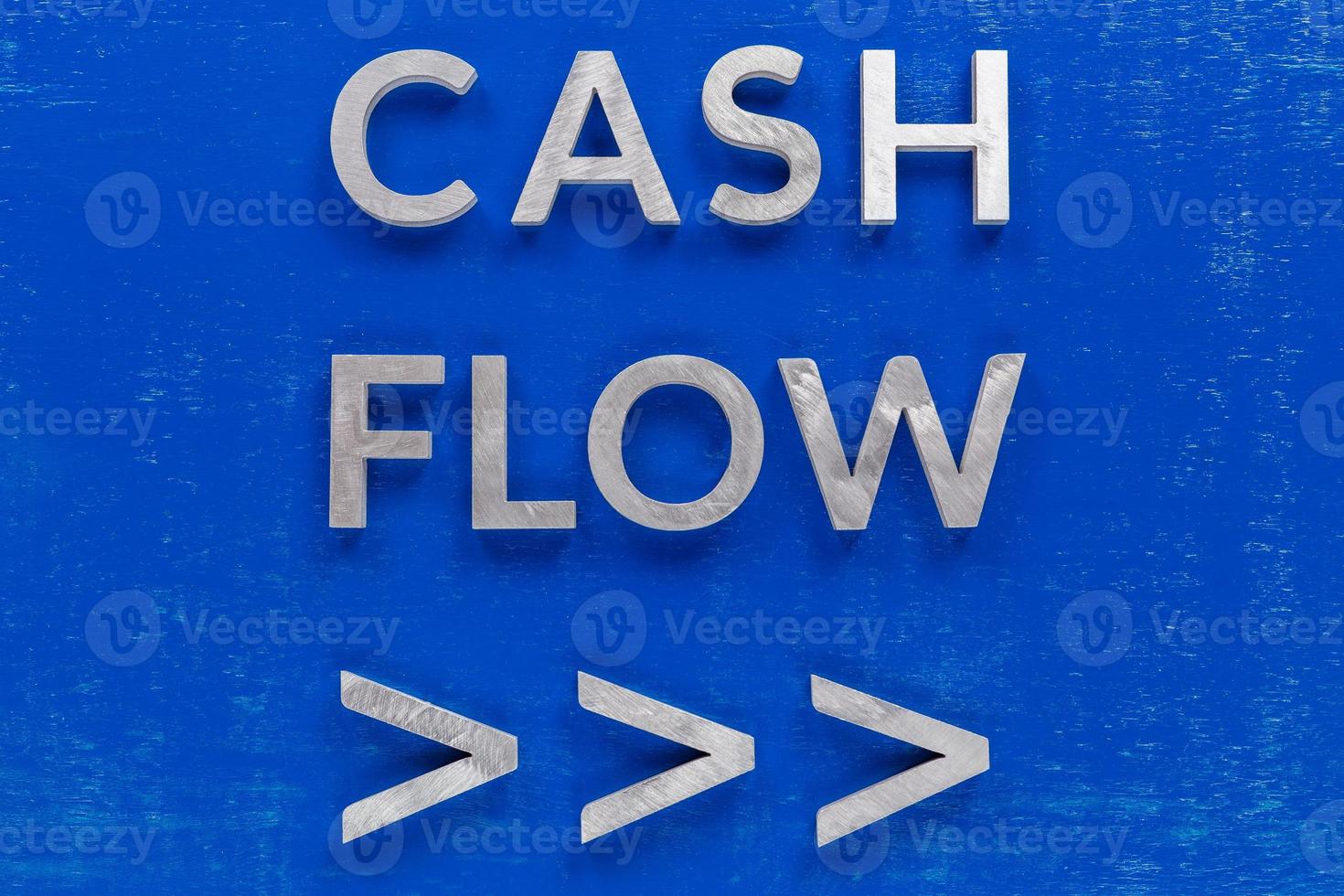 The words cash flow with arrows laid on blue painted board with thick silver metal aphabet characters. photo