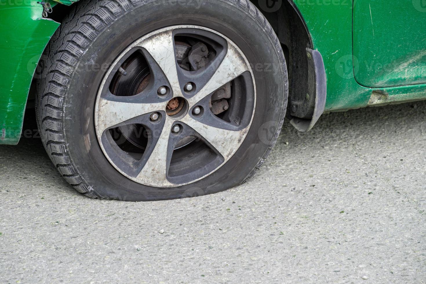 primer plano de la rueda desinflada de un coche civil verde antiguo en un día seco y soleado sobre una superficie de asfalto gris foto