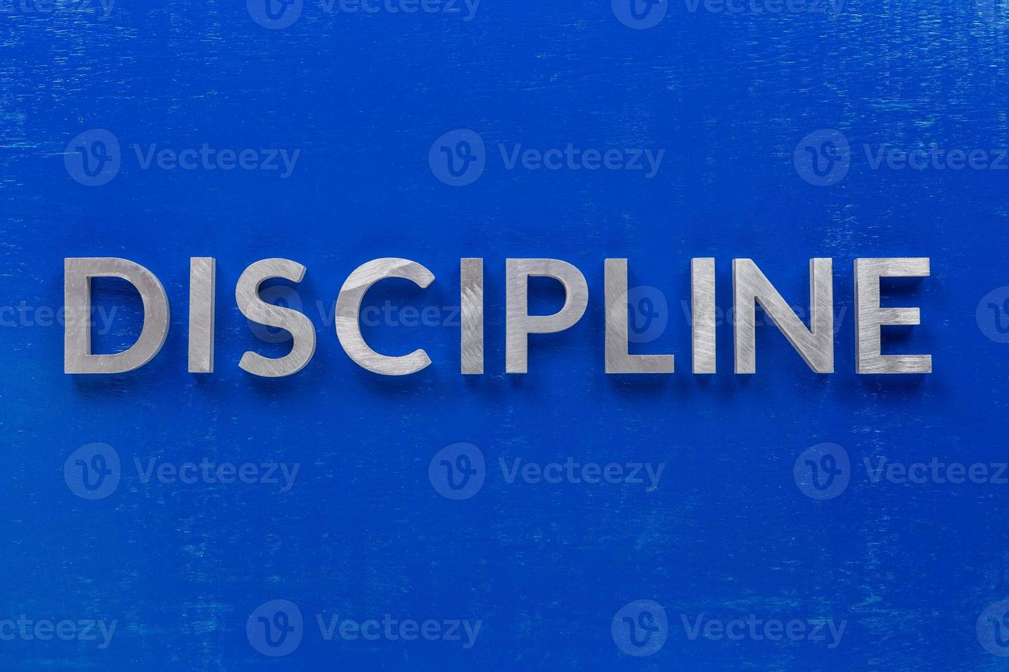 la palabra disciplina colocada con caracteres de metal plateado en una tabla de madera pintada de azul en una composición plana central foto