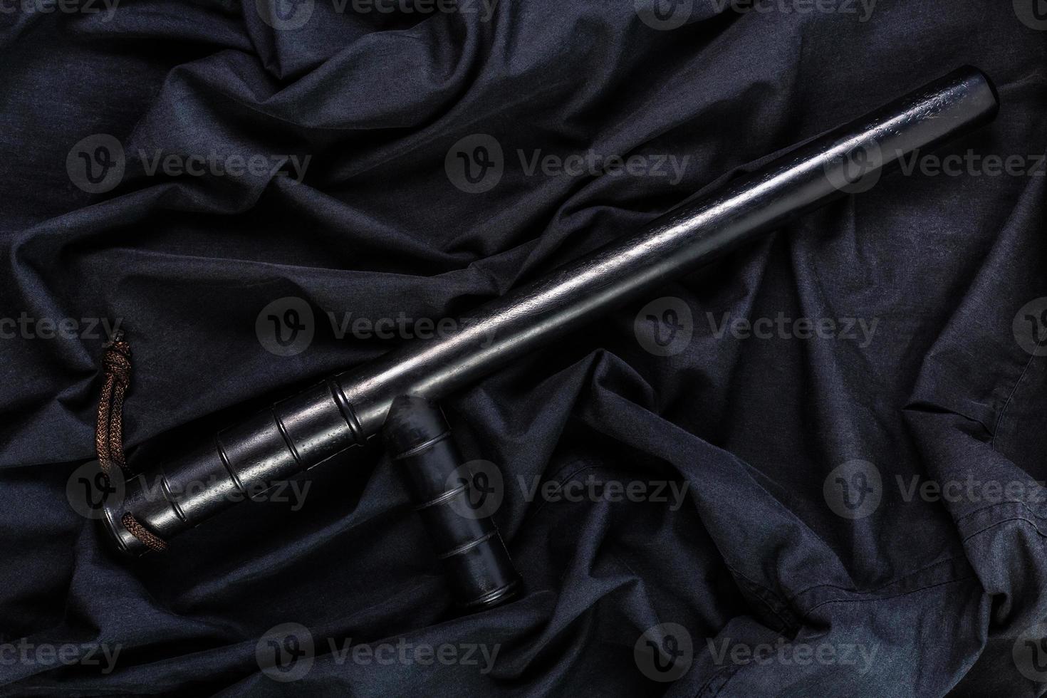 black rubber police baton on black shirt wrinkled cloth low-key flat lay photo