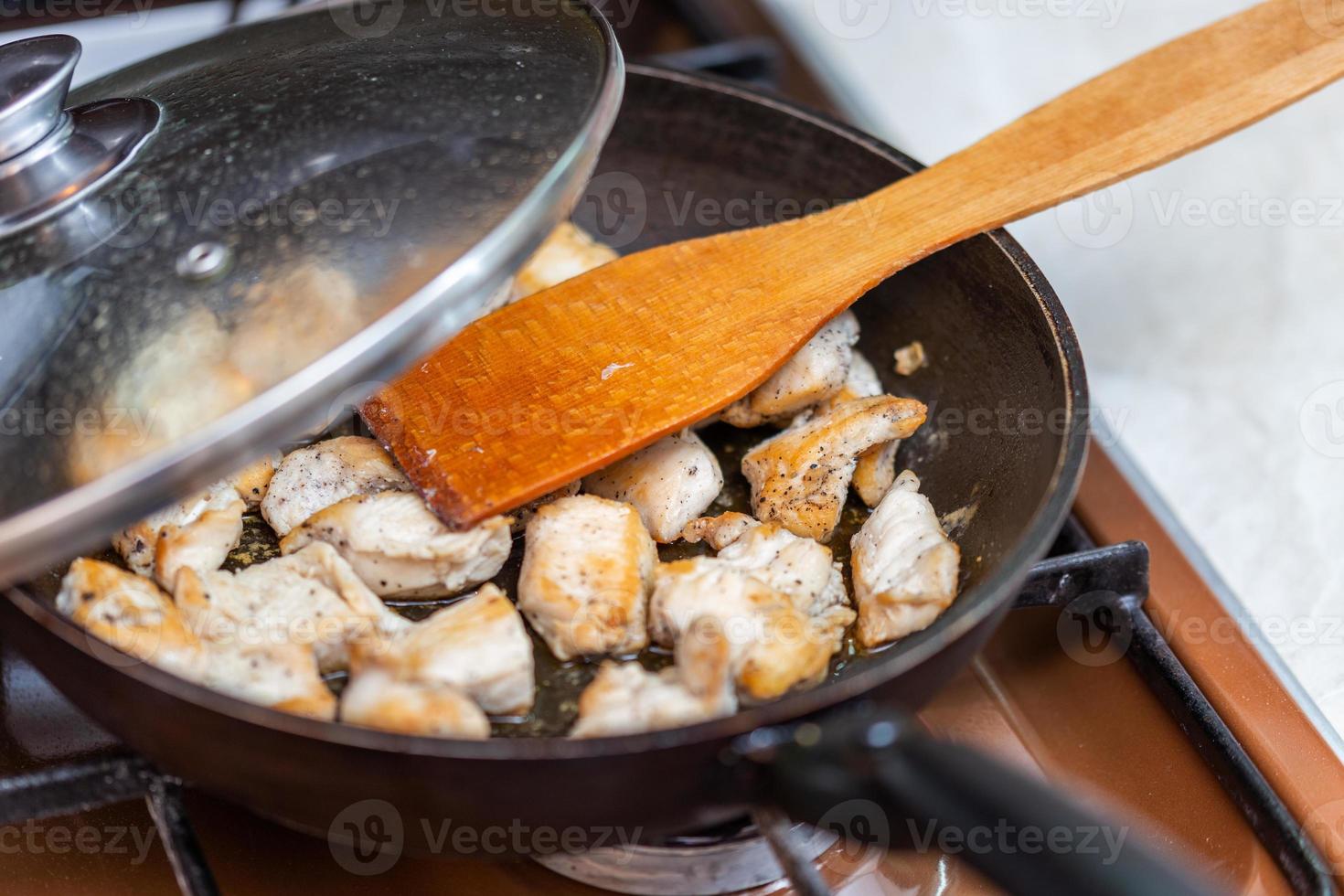fried chicken in a open pan with ground black pepper and wooden kitchen spatula photo