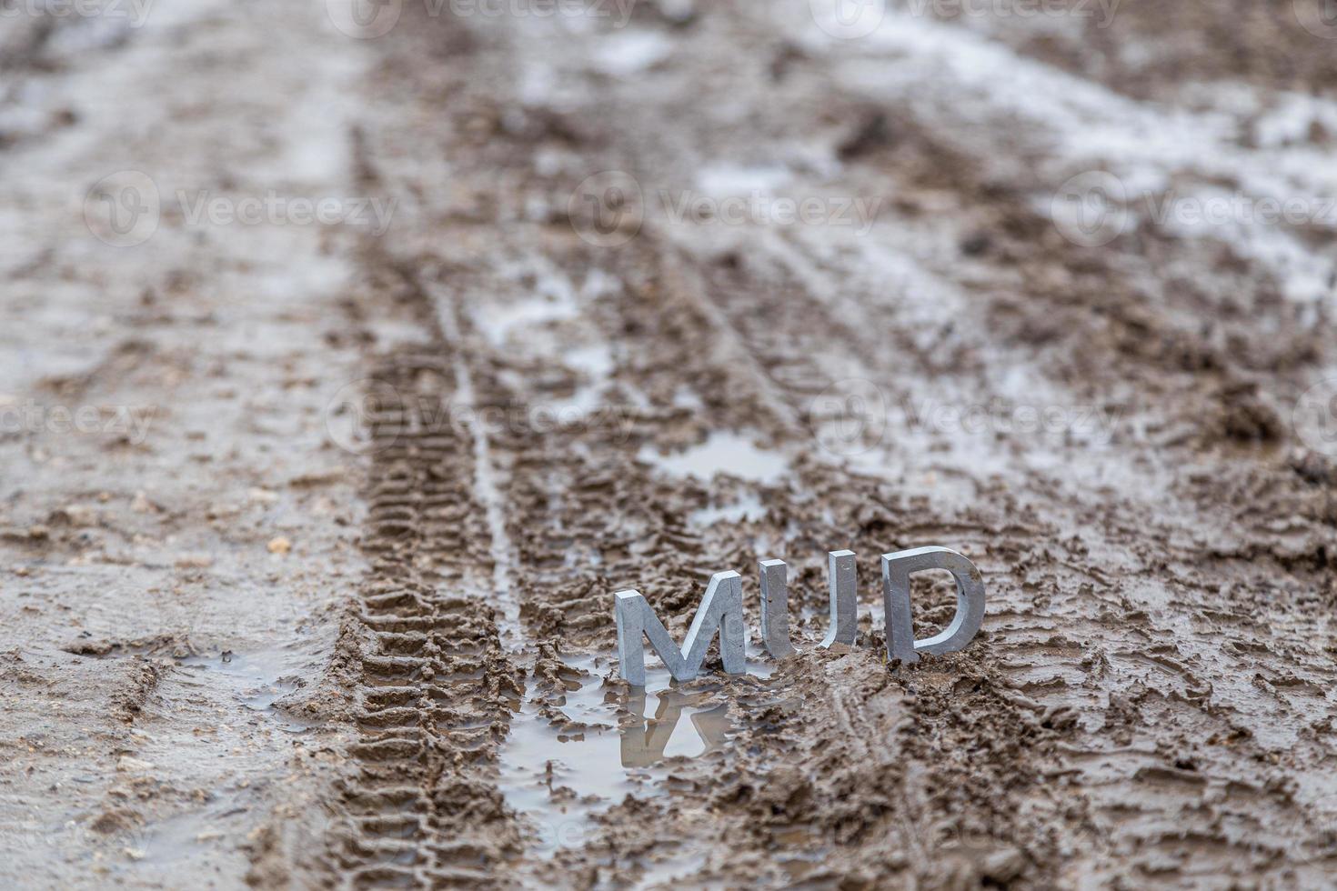 the word mud composed of silver metal letters on wet dirt surface photo