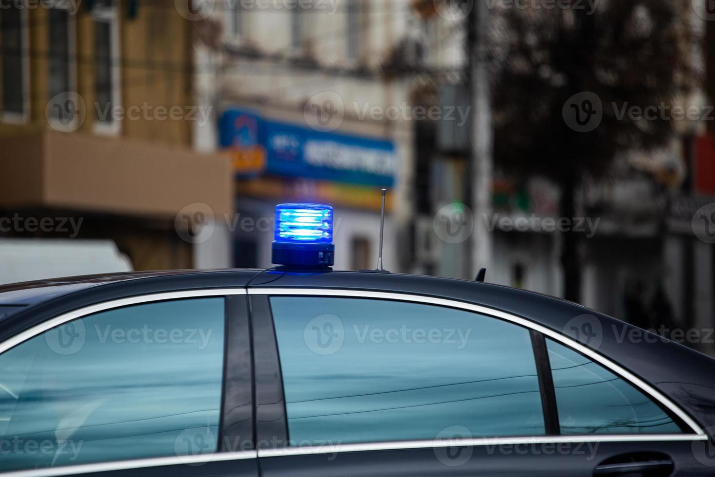 blue flashing light on top of black government car on daytime city street photo