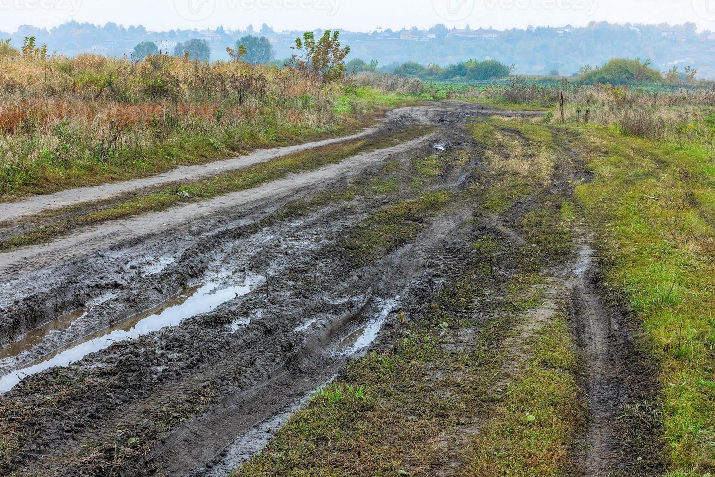 Mañana neblinosa otoñal paisaje rústico con camino de tierra en primer plano y pequeños edificios en la colina al fondo foto