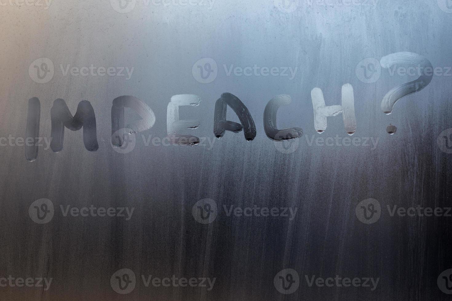 the question impeach written on wet window glass close-up with blurred background photo