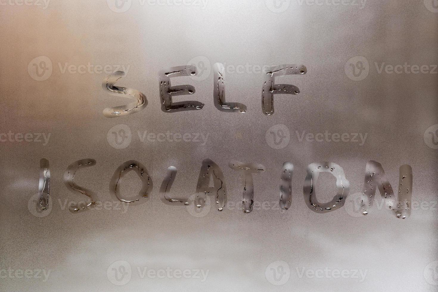 the words self isolation handwritten on wet window glass at daytime - close-up full frame picture with selective focus photo