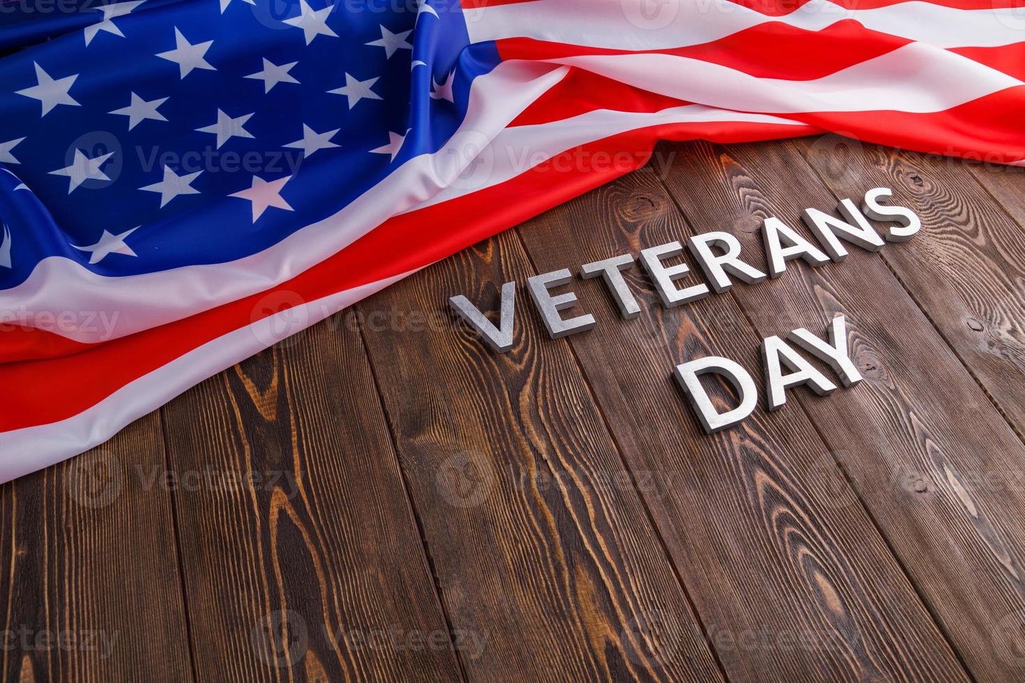 the words veterans day laid with silver metal letters on wooden board surface with crumpled usa flag photo