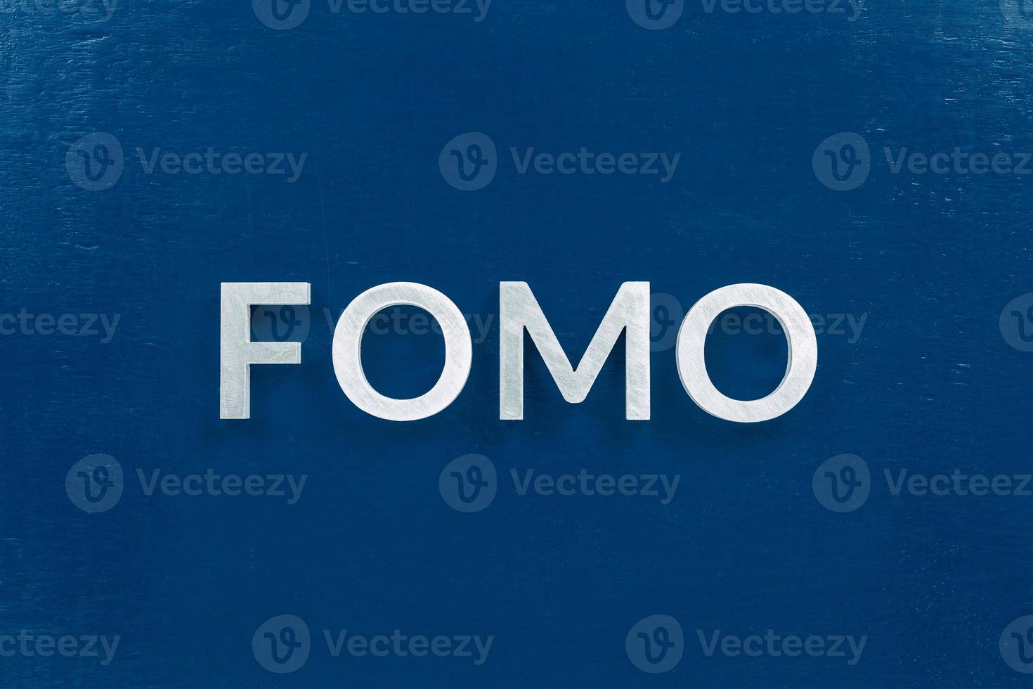 the abbreviation word fomo - fear of missing out - laid with silver letters on classic blue color flat surface photo