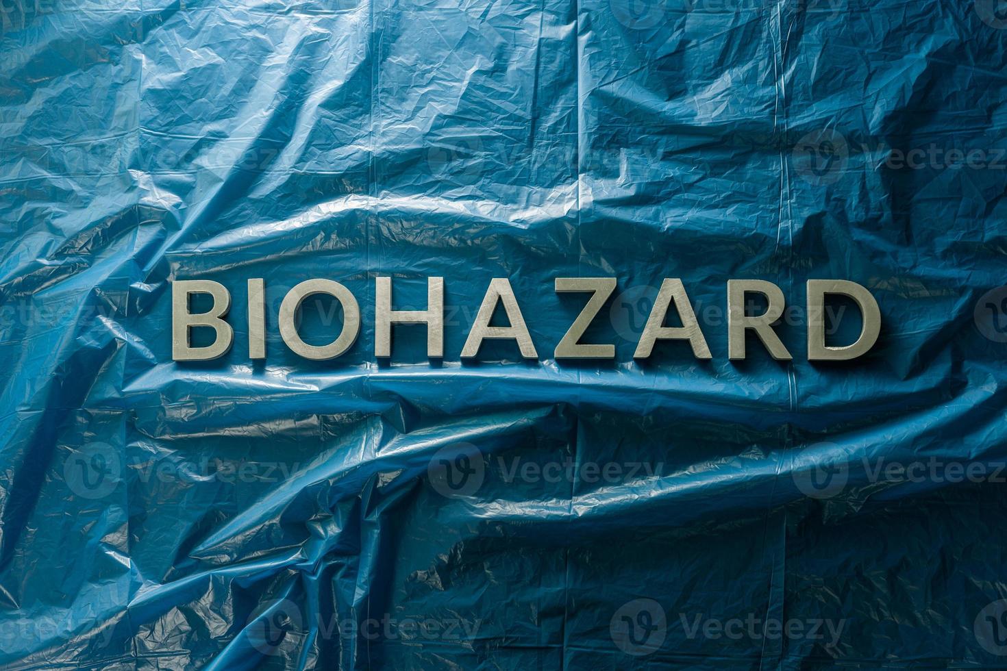 the word biohazard laid with silver letters on blue crumpled plastic film background in flat lay composition at center photo