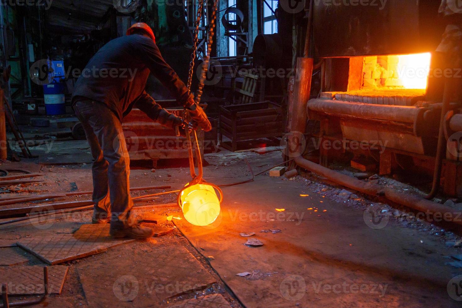 Trabajador de una fábrica de forja moviendo una pieza de trabajo de metal caliente brillante con una grúa de cadena focreps foto