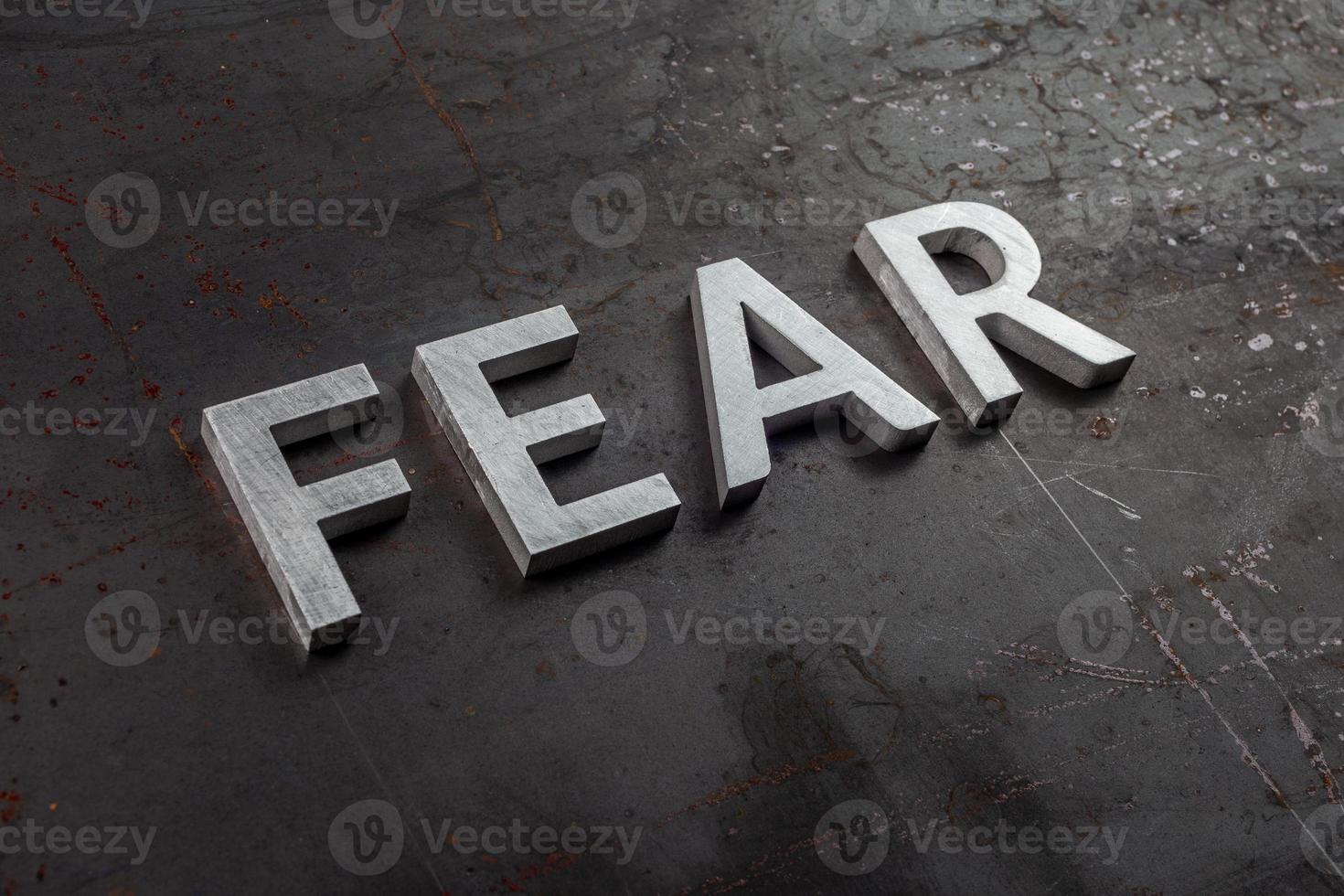 the word fear laid with silver letters on raw rusted steel sheet surface in diagonal slanted perspective photo