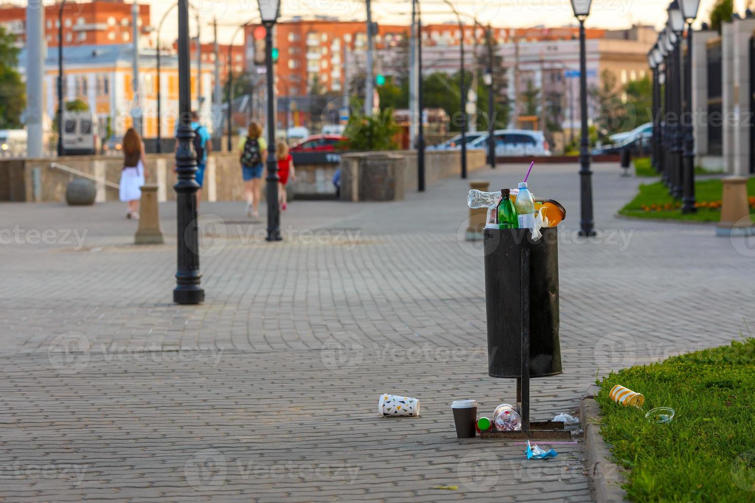 overflowing trash can on the sidewalk pavement at summer daylight photo